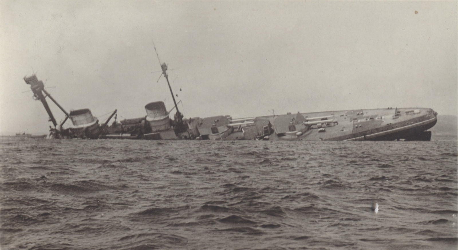 The German battlecruiser SMS Derfflinger lying capsized on its side in the water at Scapa Flow after the 1919 scuttling, masts tilted and hull mostly submerged.