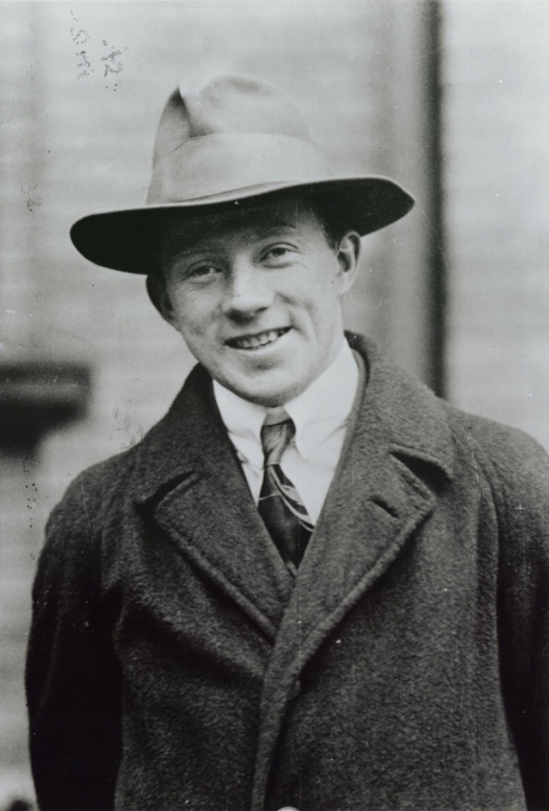 A black-and-white photograph of a young Werner Heisenberg smiling in a hat and overcoat, from the 1920s.
