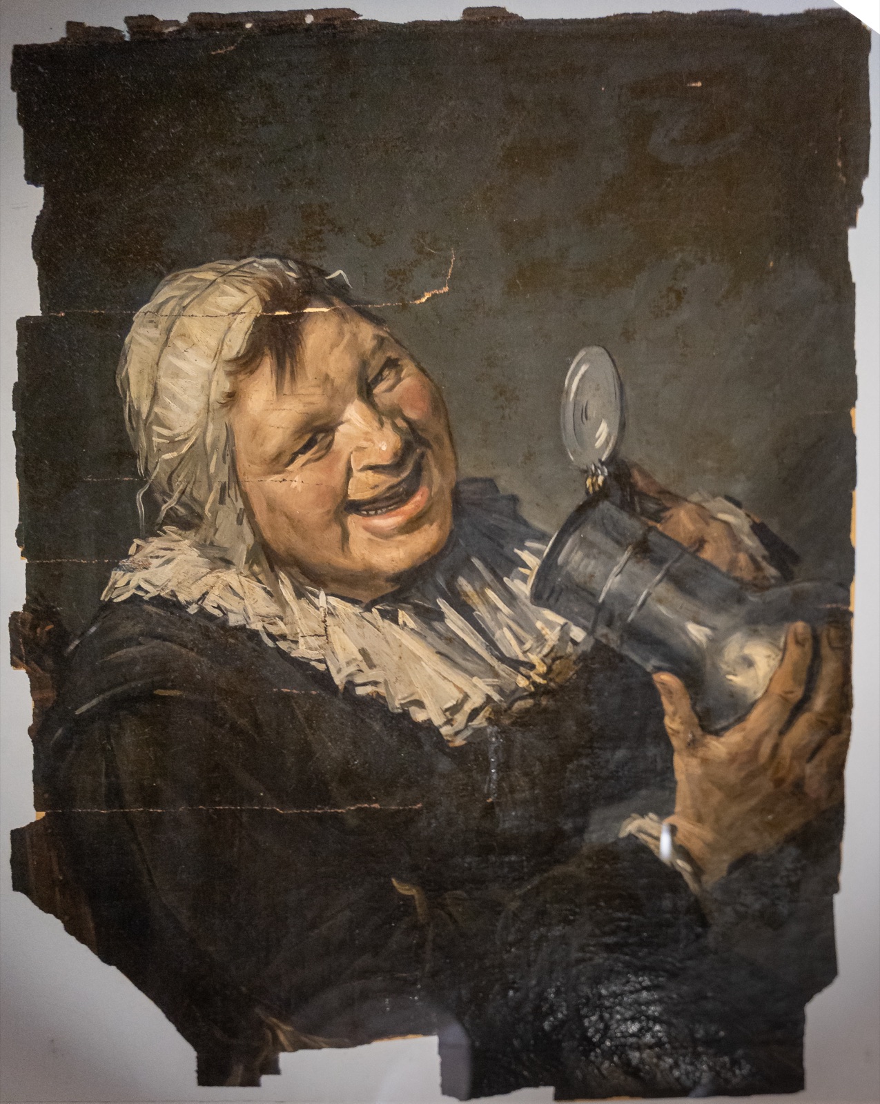Han van Meegeren’s forgery of Frans Hals’s Malle Babbe: a ragged-edged oil panel of a laughing woman in a white cap raising a pewter tankard.