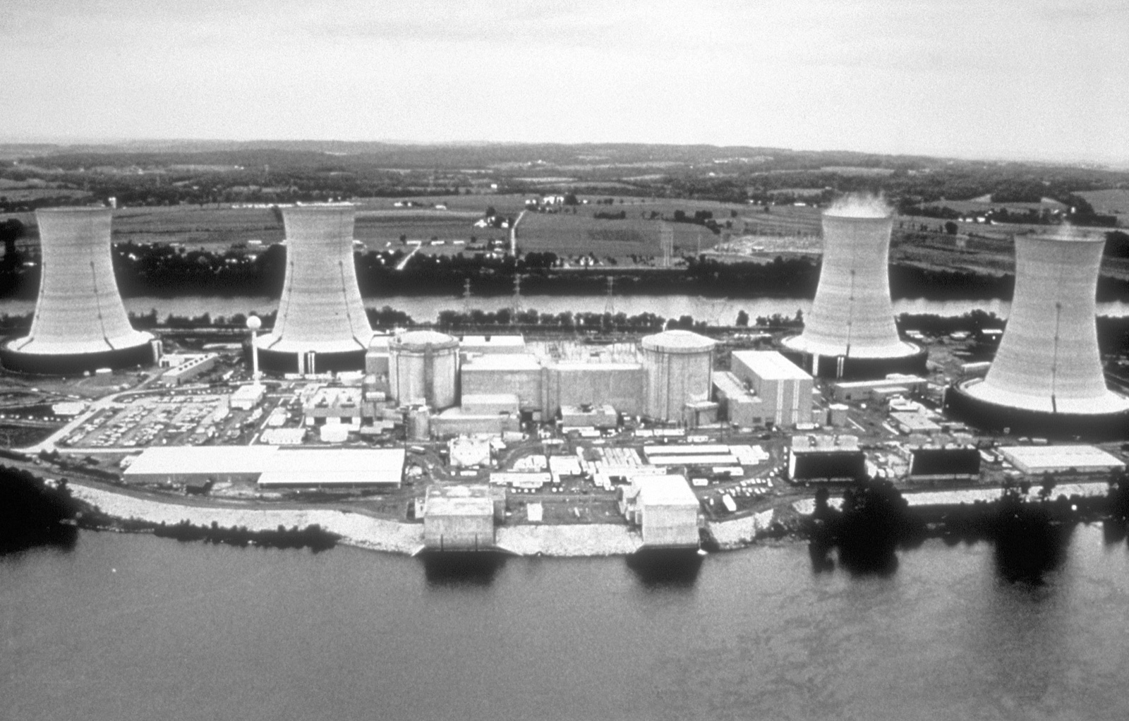 The Three Mile Island nuclear generating station: large hyperboloid concrete cooling towers and low reactor buildings on an island in a wide river.