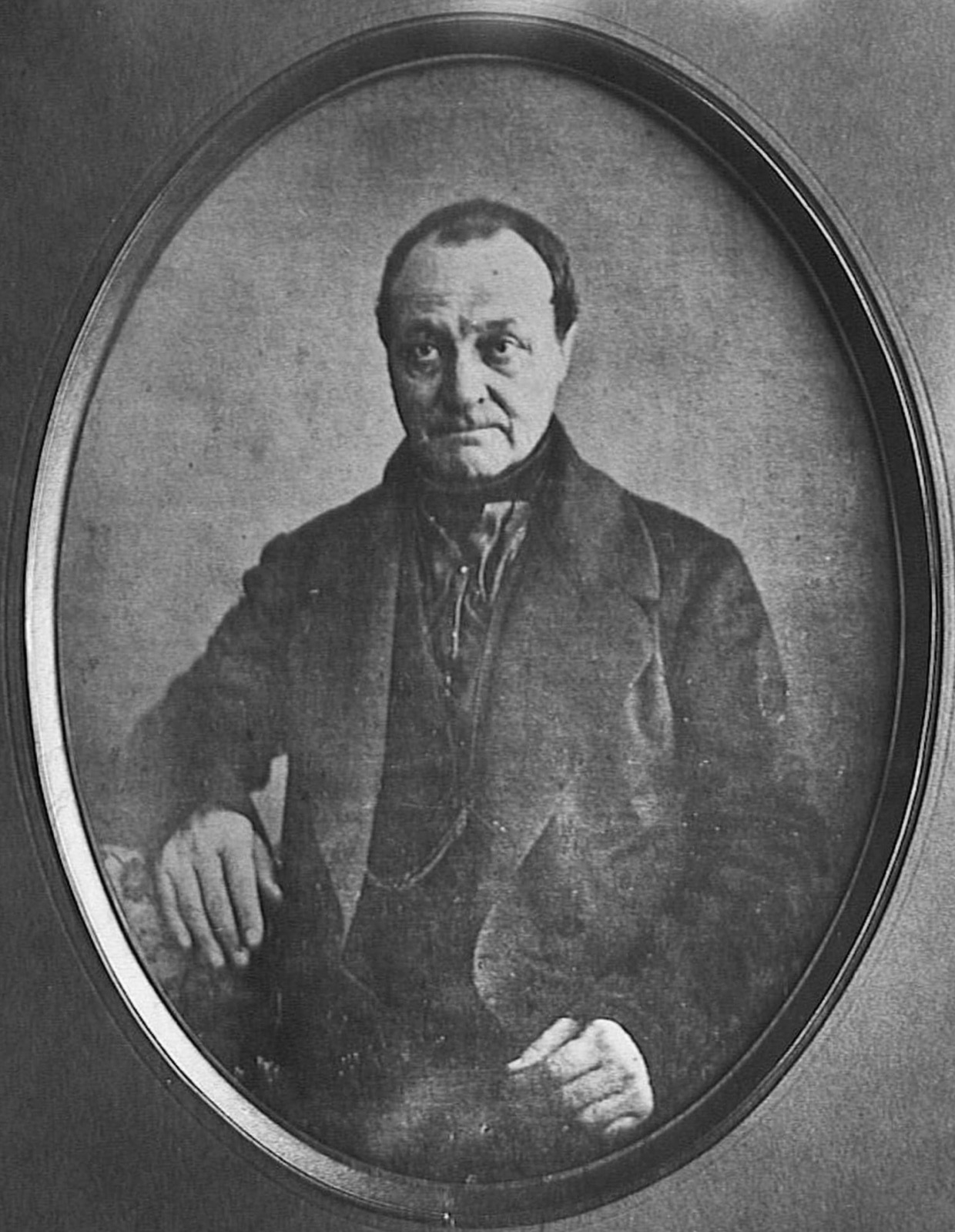 A daguerreotype portrait, in an oval mount, of the philosopher Auguste Comte seated with one arm resting on a chair back.